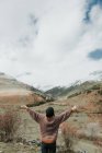 Повернення до молодої леді у светрі та капелюсі, що стоїть у мальовничому ландшафті між горами з піднятими руками у Піренеях. — стокове фото