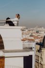 Seitenansicht einer jungen, stylischen Dame in Freizeitkleidung und Sonnenbrille, die sich auf Schienen auf dem Dach lehnt und blauen Himmel vor Stadtbild-Hintergrund in Madrid, Spanien — Stockfoto