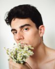 Vista lateral do jovem sem camisa com flores brancas frescas na boca olhando para a câmera no fundo borrado — Fotografia de Stock