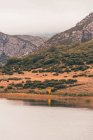 Persona en impermeable amarillo que va a la orilla del lago cerca de una montaña en Isoba, Castilla y León, España - foto de stock