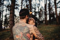 Back view of shirtless man with tattoos embracing woman in park on blurred background — Stock Photo