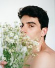 Seitenansicht des jungen Mannes ohne Hemd mit frischen weißen Blumen in den Händen, der auf verschwommenem Hintergrund in die Kamera schaut — Stockfoto