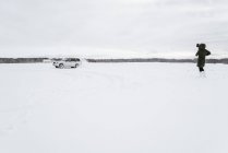 Vista posteriore della signora in abbigliamento invernale guardando l'automobile alla deriva sul prato di neve a Vilnius, Lituania — Foto stock