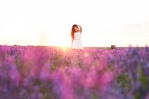 Усміхнена молода жінка в сукні під підсвічуванням між фіолетовим лавандовим полем — стокове фото