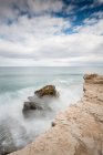 Rough stone cliff and waving stormy sea under cloudy sky — Stock Photo