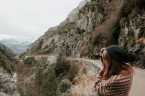 Vista laterale della giovane signora in maglione e cappello scattare foto sulla macchina fotografica tra le colline dei Pirenei — Foto stock