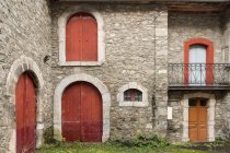 Ярд з зеленою травою між сірим кам'яним будинком з червоними дверима в Піренеях. — стокове фото
