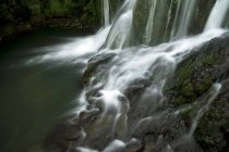 Long exposure of water stream flowing from rough gray rocks in moss into reservoir — Stock Photo