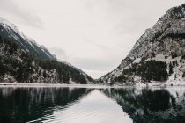 Incredibile vista della superficie dell'acqua tra alte montagne con alberi nella neve e cielo nuvoloso nei Pirenei — Foto stock