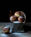 Pastel fresco cerca del juego de pan horneado en papel artesanal con azúcar en polvo en la mesa de madera en la oscuridad sobre fondo negro - foto de stock