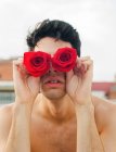 Brünette junge Mann ohne Hemd zeigt weinig frische Rosen bedecken Augen auf verschwommenem Hintergrund — Stockfoto