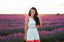 Jovem mulher sorrindo e de pé entre o campo de lavanda violeta — Fotografia de Stock