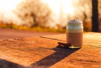 Aromatic cinnamon sticks near jar of yummy coffee with cream on lumber tabletop — Stock Photo