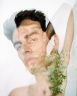 Vue latérale de jeune homme torse nu avec des fleurs blanches fraîches dans les mains en regardant la caméra sur fond flou — Photo de stock