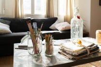 Sammlung von Pinseln und Bleistiften in Glasdosen in der Nähe von Flaschen und Materialhaufen auf niedrigem Tisch in der Nähe von Sofa im Zimmer — Stockfoto