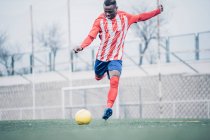 Jogador de futebol africano com equipamento vermelho e branco jogando futebol. — Fotografia de Stock