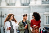 Three young friends walking and drinking coffee in the streets of Madrid on winter — Stock Photo