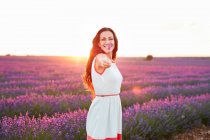 Happy attractive lady with flowers in outstretched arm between beautiful purple blooms on lavender field — Stock Photo
