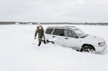 Young lady with shovel digging snow from automobile near meadow in Vilnius, Lithuania — Stock Photo