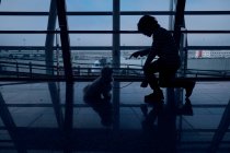 Silhouette de garçon méconnaissable dressant un petit chien à l'intérieur du bâtiment sombre de l'aéroport — Photo de stock