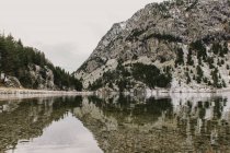 Amazing view of water surface between high mountains with trees in snow and cloudy heaven in Pyrenees — Stock Photo