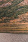Personne en imperméable jaune sur la rive d'un lac près de Wigwam et colline à Isoba, Castille et Léon, Espagne — Photo de stock