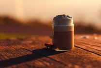 Aromatische Zimtstangen neben Glas leckeren Kaffees mit Sahne auf Holztisch — Stockfoto