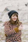 Atractiva joven en suéter y sombrero con las manos cruzadas cerca de la colina sobre fondo borroso en los Pirineos - foto de stock