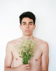 Vue latérale de jeune homme torse nu avec des fleurs blanches fraîches dans les mains en regardant la caméra sur fond flou — Photo de stock