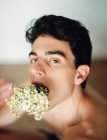 Side view of young shirtless guy with fresh white flowers in mouth looking at camera on blurred background — Stock Photo