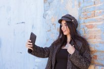 Чарівні латиноамериканських леді беручи selfie з мобільним телефоном перед пошарпаний стіні — стокове фото