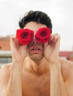 Brunette young shirtless guy showing vinous fresh roses covering eyes on blurred background — Stock Photo