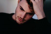 Closeup young thoughtful guy in black sweater with hand on hairs looking downstairs in Madrid, Spain — Stock Photo