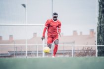 Jogador de futebol africano com roupa vermelha jogando futebol. — Fotografia de Stock