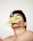 Jovem sem camisa cara com flores brancas frescas na boca olhando para a câmera no fundo borrado — Fotografia de Stock
