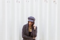 Stylish Hispanic lady in coat and cap posing against white wall — Stock Photo