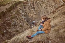 Mignon garçon assis sur la colline près du ruisseau — Photo de stock