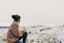 Seitenansicht einer jungen Frau in Pullover und Hut mit Becher und Blick auf die schneebedeckten Hügel in den Pyrenäen — Stockfoto