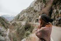 Vista lateral de la joven dama en suéter y sombrero tomando fotos en cámara entre colinas en los Pirineos - foto de stock