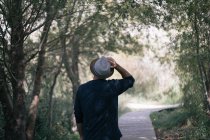 Вид ззаду чоловіка торкається капелюха, стоячи на алеї в парку — стокове фото