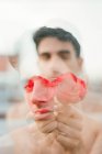 Brunette young shirtless guy showing vinous fresh roses and looking at camera on blurred background — Stock Photo