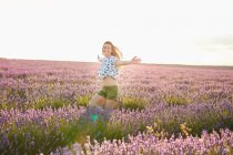 Young woman running between violet lavender field at sunset — Stock Photo