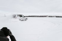 Back view of crop guy shooting on camera automobile drifting on snow meadow and cloudy sky in Vilnius, Lithuania — Stock Photo