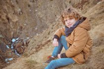Милый мальчик, сидящий на холме возле ручья — стоковое фото