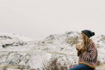 Seitenansicht einer jungen Frau in Pullover und Hut mit Becher und Blick auf die schneebedeckten Hügel in den Pyrenäen — Stockfoto