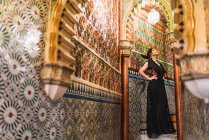 Вид сбоку на страстную молодую женщину в платье, стоящую в узком коридоре, украшенном мозаикой — стоковое фото
