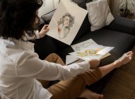 Mulher desenhando em papéis no sofá no quarto — Fotografia de Stock