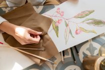 Обрізане зображення жінки з матеріалом за столом з фарбою на листі, олівцями та пензлями — стокове фото