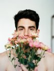 Brunette young shirtless guy holding rose fresh flowers looking at camera on grey background — Stock Photo