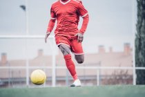 Африканский футболист в красном костюме играет в футбол. — стоковое фото